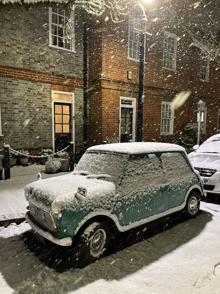 A snowed classic Mini electric conversion, complete with modern electric drivetrain and battery pack, parked in London.